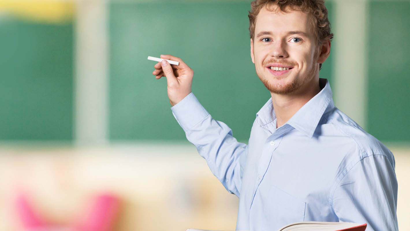 Professor com livro e giz na mão sorri